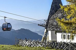 Kleine Bergkapelle mit Schindeldach bei der Kraftalm in Itter, daneben verläuft die Gondelbahn der Salvistabahn, umgeben von Almwiesen und Bergpanorama im Sommer.