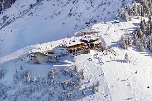 Verschneite Bergstation mit moderner Architektur im Skigebiet, umgeben von Skipisten, Gondeln und Skifahrern in winterlicher Hochgebirgslandschaft