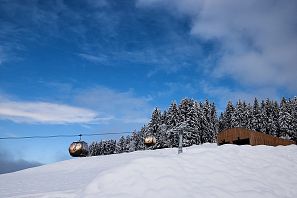 Zwei goldene Gondeln fahren über eine verschneite Winterlandschaft mit schneebedeckten Bäumen unter blauem Himmel