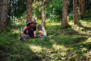 Hexe und Kind sitzen im Wald und entdecken die Insekten.