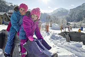 Kinder sitzen im Winter auf einem Holzschwein.