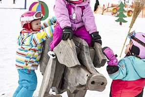 Kinder spielen auf einem Holztier im Winter.