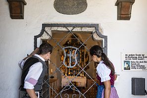 Zwei traditionell gekleidete Personen die in die Kapelle auf der Hohen Salve schauen.