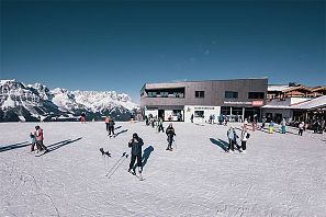 Skifahrer und Wintersportler versammeln sich bei Sonnenschein vor der modernen Bergstation der Hartkaiserbahn mit Blick auf das verschneite Bergpanorama