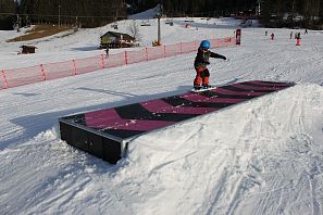 Kleinkind fährt auf einem Snowboard über ein Hindernis.