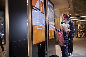Kind benützt das Touch Display für das Self Checkin beim Skiverleih Sporthaus Edinger während die Mutter zusieht