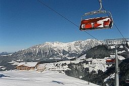 Siller Keat Sessellift mit geschlossener orangen Kuppel verschneit.