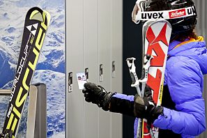 Frau in Skikleidung steht vor Spinden mit ihren Ski.