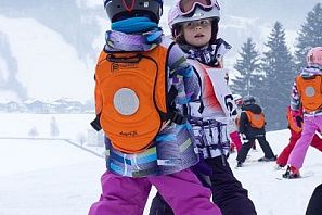 Kinder mit orangen Rucksäcken auf der Skipiste.