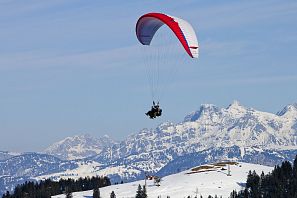 Rot-weißer Paragleiter bei einem Tandemflug im Winter in der Luft über der SkiWelt