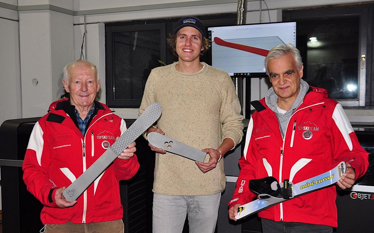 Drei Herren, zwei mit roter Skijacke und ein Herr in der Mitte mit beigem Pullover und Kappe halten jeweils kleine Mini Carver in den Händen