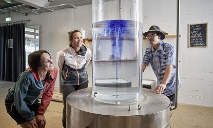 Drei Erwachsene beobachten einen Zylinder mit Wasser im &#39;Blauen Wunder&#39; im Hexenwasser Söll.