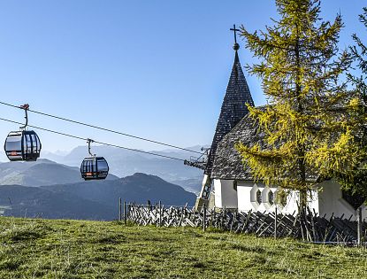 Kapelle mit Ausblick auf Berge und Gondeln.
