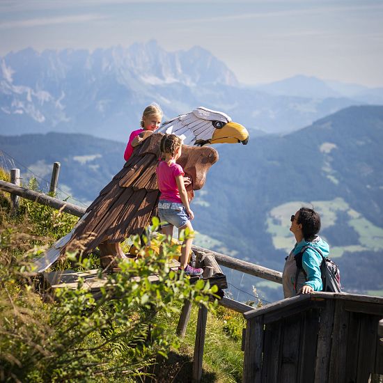 Mutter mit zwei Kindern in der Natur betrachten einen Adler aus Holz.