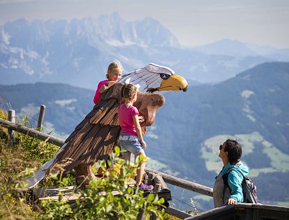 Mutter mit zwei Kindern in der Natur betrachten einen Adler aus Holz.
