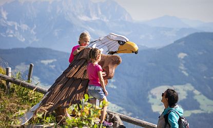 Mutter mit zwei Kindern in der Natur betrachten einen Adler aus Holz.