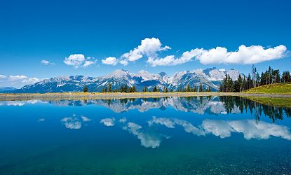 Sicht vom klaren Astbergsee auf eine Bergkulisse und strahlend blauem Himmel.