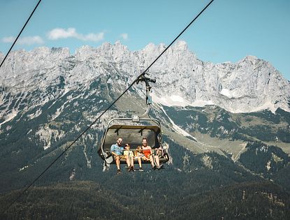 Leute in einem Sessellift vor dem Wilden Kaiser.