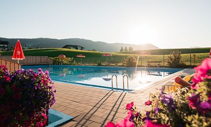 Poolanlage im Sommer in Naturlandschaft mit violetten Blumen und roten Eskimo Sonnenschirmen