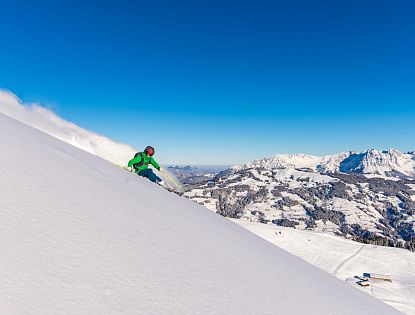 Freerider mit grüner Jacke im frischen Pulverschnee zieht erste Spuren mit Panoramablick im Hintergrund