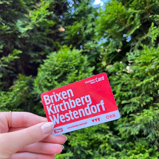 Frauenhand hält Gästekarte Kitzbuehler Alpen mit Aufschrift Brixen Kirchberg Westendorf