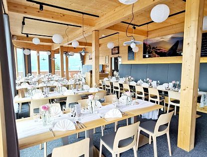 Modernes, lichtdurchflutetes Restaurant mit Holzelementen, weißen Papierlampions und elegant gedeckten Tischen für eine Feier