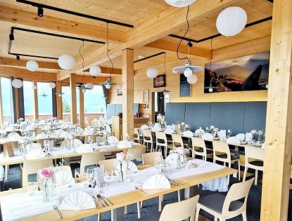 Modernes, lichtdurchflutetes Restaurant mit Holzelementen, weißen Papierlampions und elegant gedeckten Tischen für eine Feier