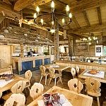 Innenansicht einer urigen Almhütte mit rustikalen Holzmöbeln, geschnitzten Stühlen und stimmungsvoller Beleuchtung durch Kronleuchter