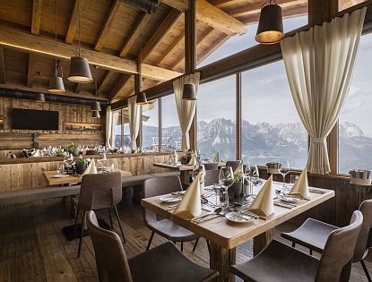 Das stilvoll gedecktes Bergrestaurant Kaiserlounge am Hartkaiser mit großen Panoramafenstern, durch die ein beeindruckender Blick auf das majestätische Kaisergebirge fällt. Die Einrichtung aus Holz schafft eine gemütlich-alpine Atmosphäre