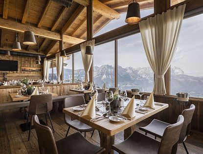 Das stilvoll gedecktes Bergrestaurant Kaiserlounge am Hartkaiser mit großen Panoramafenstern, durch die ein beeindruckender Blick auf das majestätische Kaisergebirge fällt. Die Einrichtung aus Holz schafft eine gemütlich-alpine Atmosphäre