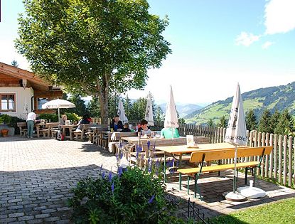 Gastgarten mit Tischen, Bänken und Sonnenschirmen des Gasthofes Kandleralm in Brixen im sommer