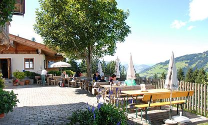 Gastgarten mit Tischen, Bänken und Sonnenschirmen des Gasthofes Kandleralm in Brixen im sommer