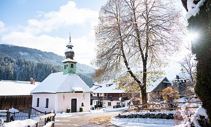 Verschneite Ortschaft Kelchsau im Winter, Kapelle und kahler großer Baum bei Sonnenstrahlen