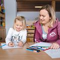 Ein Mädchen und eine Erzieherin sitzen an einem Tisch in der Kinderbetreuung und malen gemeinsam mit Buntstiften