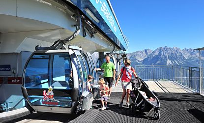 Familie mit zwei Kindern und Kinderwagen steigen aus der Gondel bei der Bergstation aus im Sommer