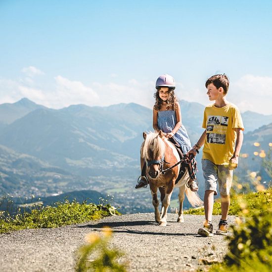 Mädchen reitet auf einem Pony und Bruder achtet auf sie.