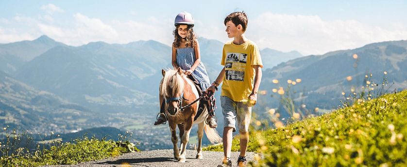 Mädchen reitet auf einem Pony und Bruder achtet auf sie.