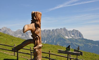 Geschnitzte Figur vor einer Bergkulisse.