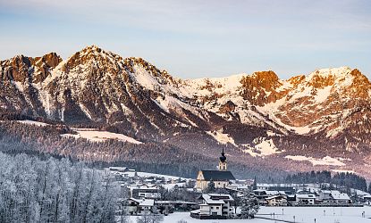 Blick auf das Dorf Söll mit Kirche und einer beeindruckend verschneiten Bergkulisse im Hintergrund.
