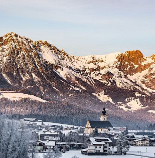 Blick auf das Dorf Söll mit Kirche und einer beeindruckend verschneiten Bergkulisse im Hintergrund.