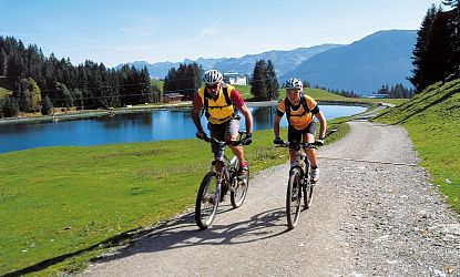 Mountainbiker fahren auf eienm schönen Wegvorbei an einem See.